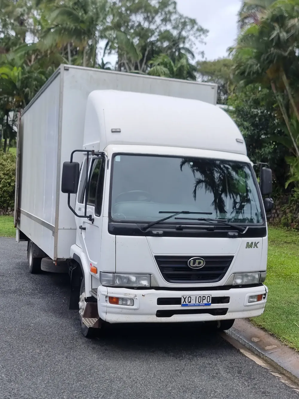 White box truck parked on a driveway surrounded by tropical trees